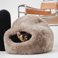 Cat peeking out from a fluffy sheepskin  pet bed on a white surface with a chair in the background. | Natural, non‑toxic pet nest for cats and small dogs | Cozy, handmade pet furniture, natural wool and sheepskin

