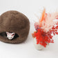 Brown sheepskin cat bed with a cat peeking out on a white background, next to a vase with red and pink flowers. | Natural, non‑toxic pet nest for cats and small dogs | Cozy, handmade pet furniture, natural wool and sheepskin

