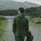 A person in a green, Waterproof Baby/Kid Clothing Set - Khaki from MellowConceptStore walking towards a lake with mountains in the background.