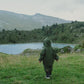 A child in a Waterproof Baby/Kid Clothing Set - Khaki from MellowConceptStore stands on a grassy field, facing a mountainous landscape with a clear blue lake.