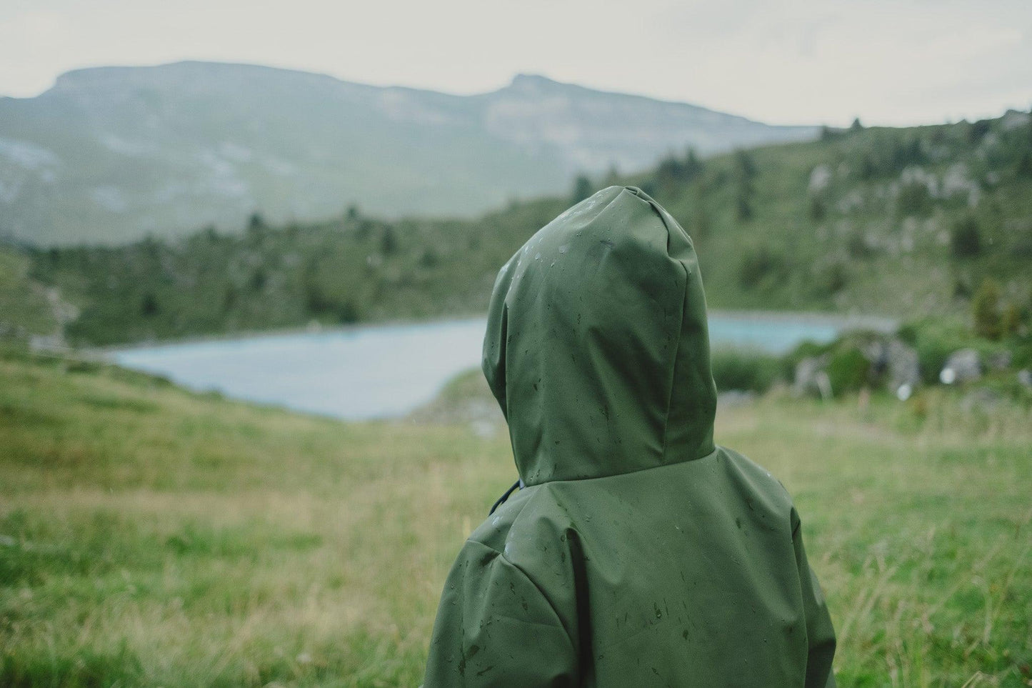 A person in a MellowConceptStore Waterproof Baby/Kid Clothing Set in Khaki gazes out at a mountainous landscape with a lake in the distance.