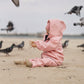 A child in a Waterproof Baby/Kid Clothing Set - Rosa from MellowConceptStore is sitting on a sandy beach surrounded by pigeons in flight and on the ground.
